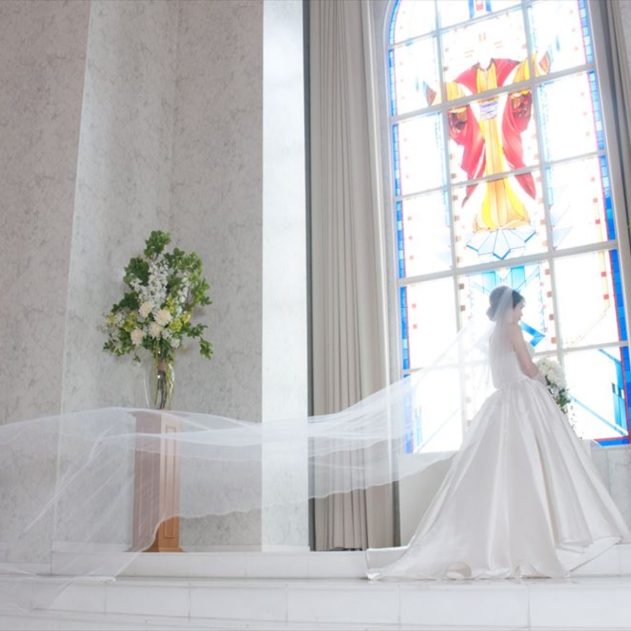 ステンドグラスから差す自然光が、純白のドレスを纏った花嫁を包み込む神秘的な空間